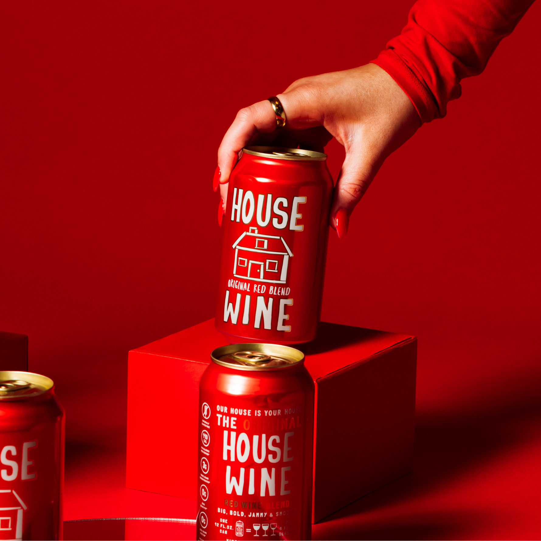 Hand holding a red can of 'House Wine' against a red background